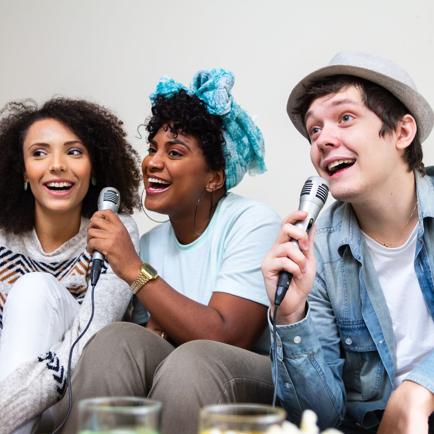 Three friends smiling and singing karaoke together, holding microphones and enjoying themselves.